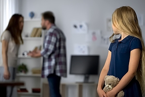 girl holding teddy bear watches parents arguing