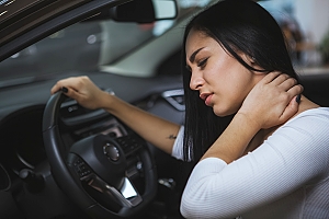 woman behind wheel rubbing neck due to pain