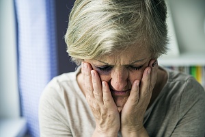 women suffering from elder abuse holding her face with her hands looking down