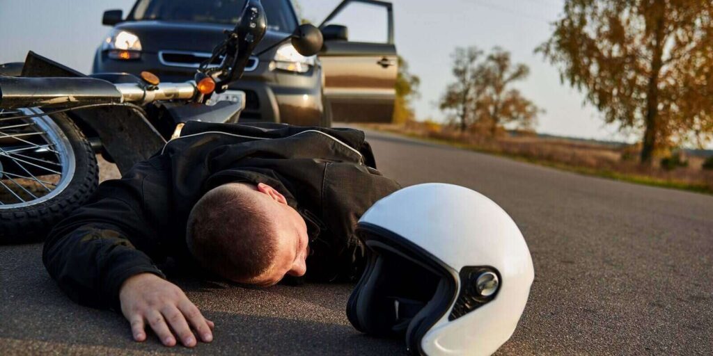 CA motorcyclist lies on the asphalt near a motorcycle and car